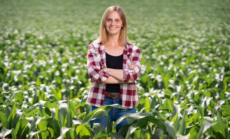 Landwirtin steht in der Mitte eines grünen Maisfeldes